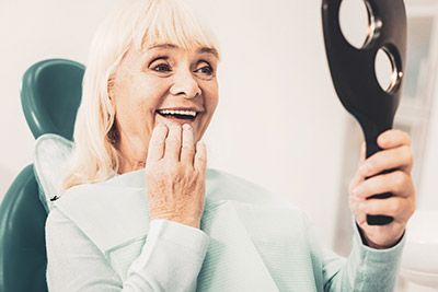 woman looking in the mirror after getting dental implants to restore her smile